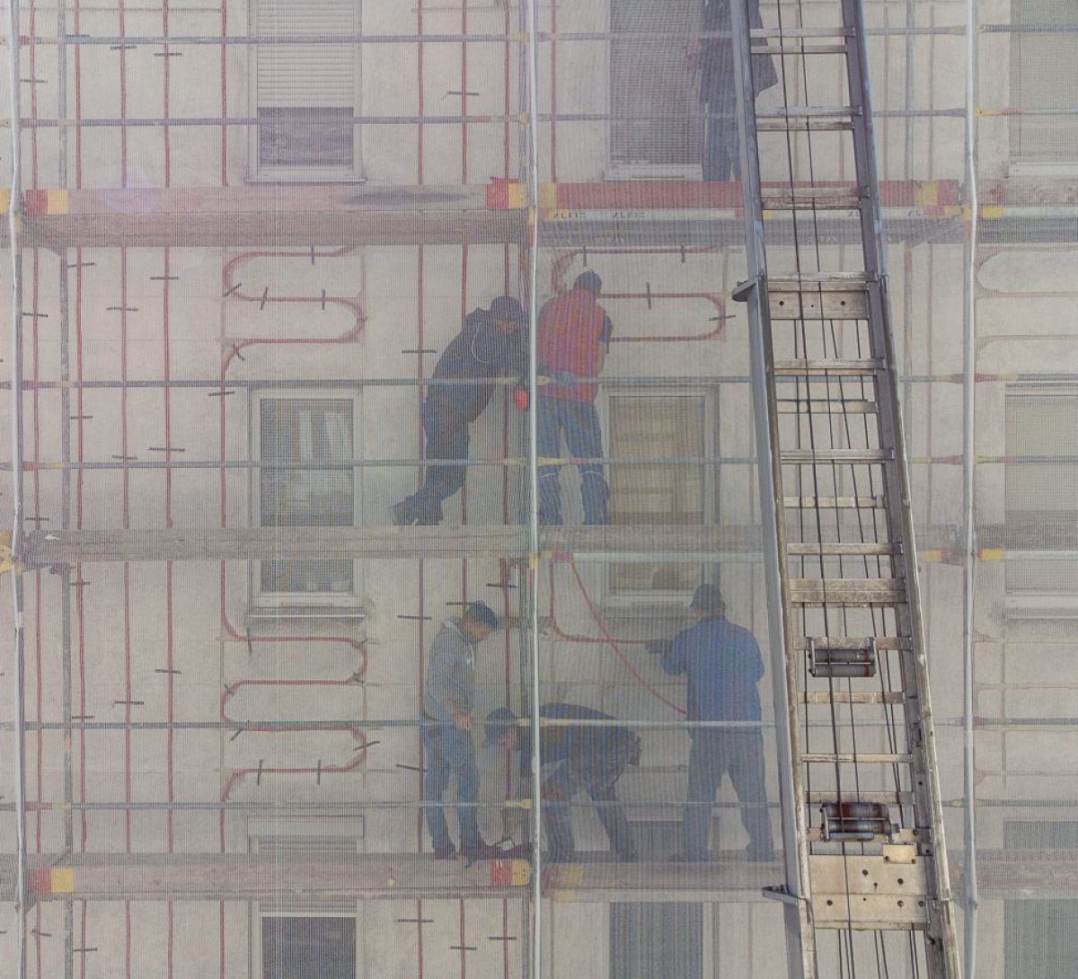 Handwerker auf Gerüsten bringen Heizschläuche außen an der Fassade eines Wohnhauses an.