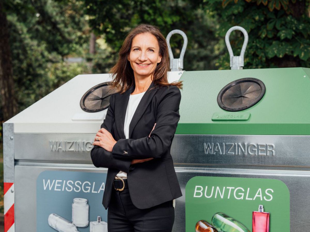 DI Eva Koller, Geschäftsführerin von Austria Glasrecycling, steht mit verschränkten Armen und stolz lächelnd vor einem der neuen Sammelcontainer für Weissglas und Buntglas.